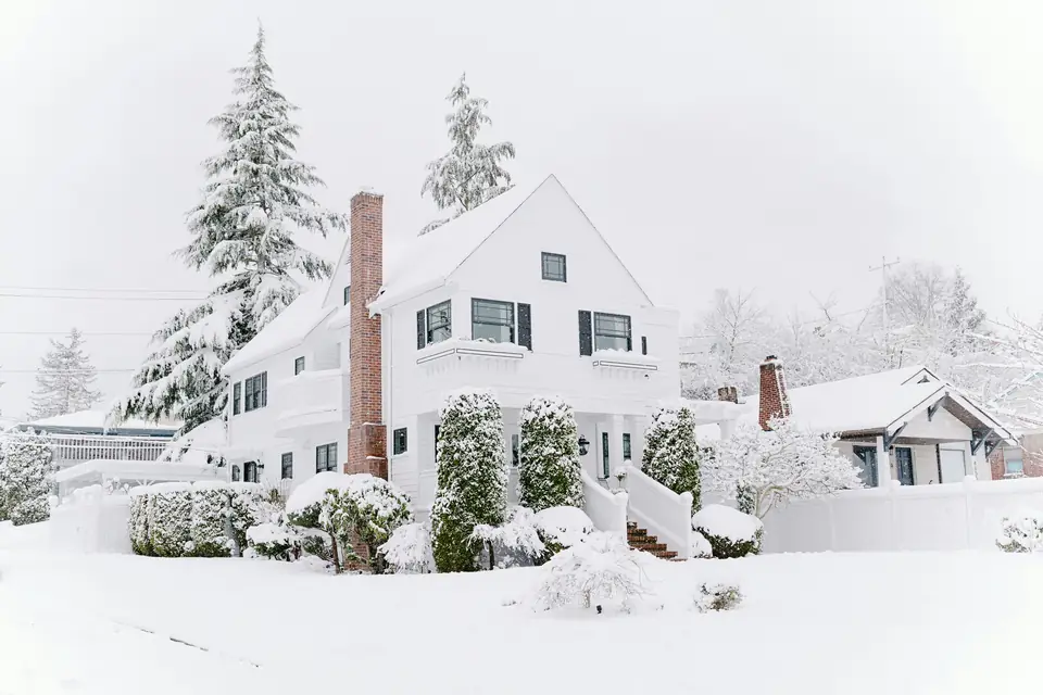 An older two-story wood-sided house with a brick chimney after a heavy snowfall